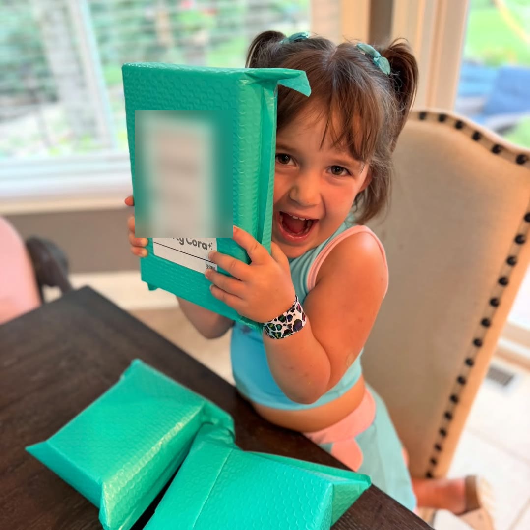 A child grinning while holding a turquoise Crafty Cora package